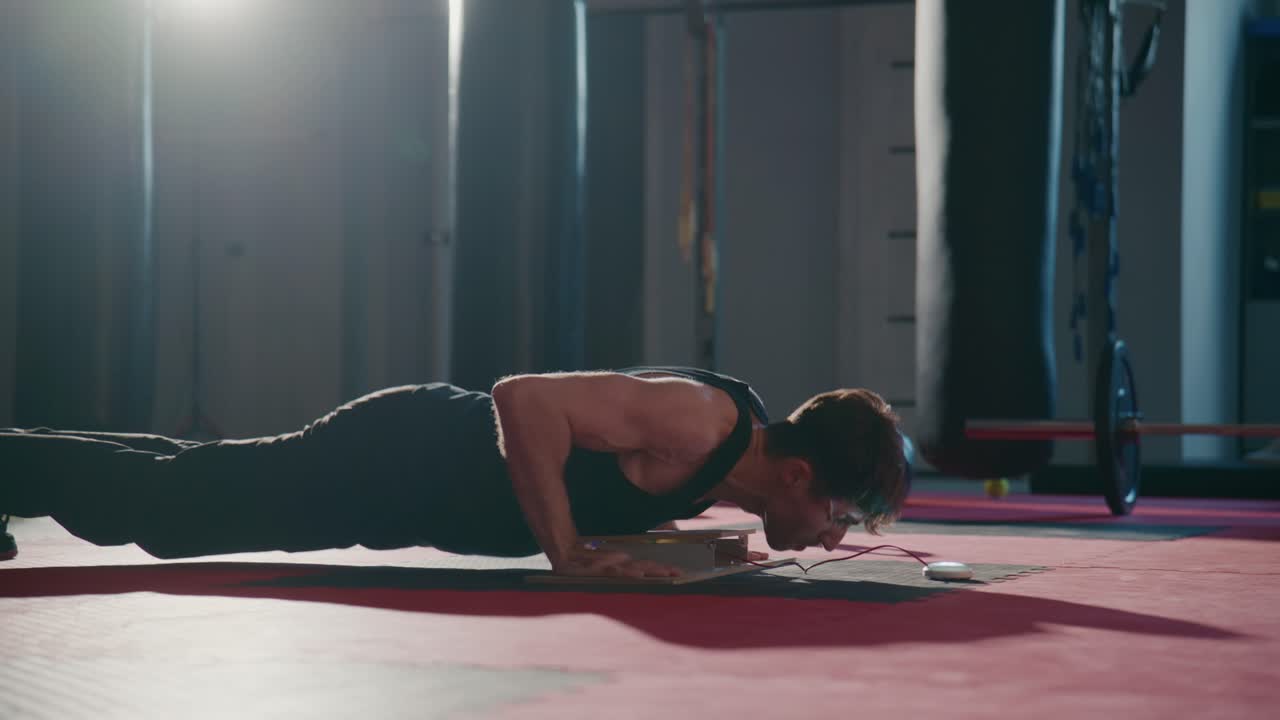 Giovane uomo che fa flessioni in una palestra con controluce.