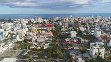 Die-Drohne-Fliegt-über-Eine-Stark-Befahrene-Straße,-Die-Von-Wolkenkratzern-Umgeben-Ist,-In-Richtung-Ozean-In-Der-Antenne-Der-Dominikanischen-Republik-Santo-Domingo