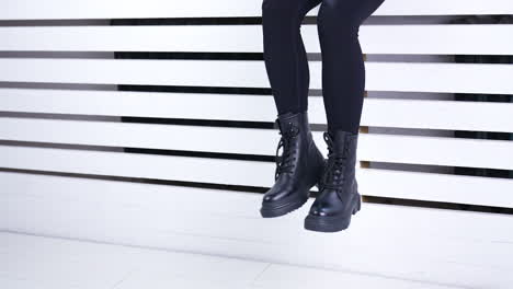 unrecognized female in black tight pants and heavy boots sitting on a window sill. model demonstrating fashionable autumn footwear.