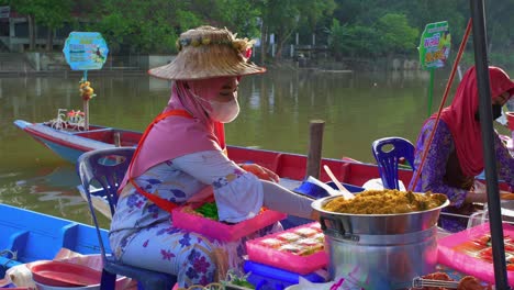 static close up of woman with mask and hat preparing asian street food packs for selling in the banks of river