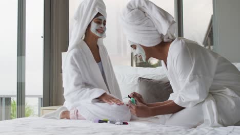 video of happy diverse female friends moisturizing with face masks and painting nails