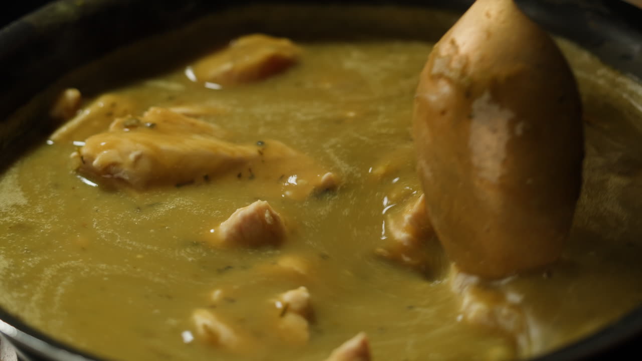 Green boiling sauce with chicken texture close-up macro. Cooking green chicken curry with spices by wooden spoon at home.