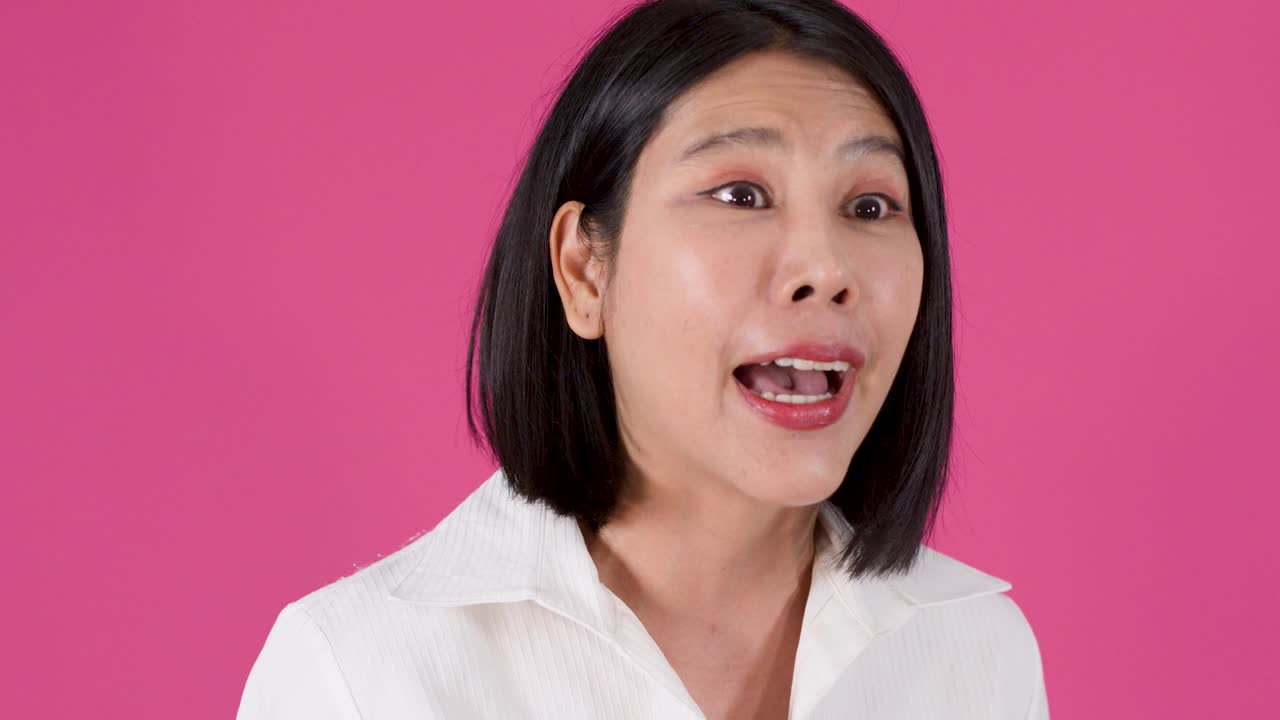 Medium shot of an expressive Asian woman talking and gesturing against a solid pink background