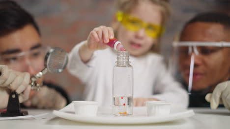 student adds red paint into clear water at science lesson