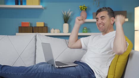 el hombre que mira la computadora portátil en casa se regocija con el éxito.
