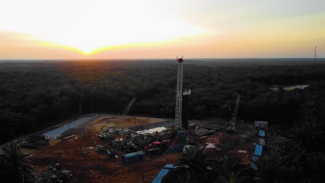 imágenes cinematográficas de drones de 4k de la estructura del equipo de la plataforma de perforación en tierra para la exploración y explotación de petróleo en medio de la jungla rodeada de palmeras durante la puesta de sol y el alto precio del petróleo