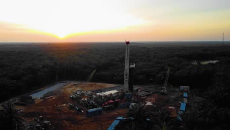 cinematic 4k drone footage of onshore drilling rig equipment structure for oil exploration and exploitation in the middle of jungle surrounded by palm oil trees during sunset and high oil price