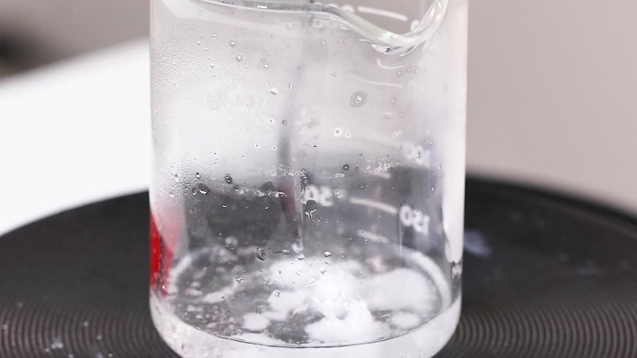 Watch the detailed process of crystal formation in a beaker with a stirring rod.