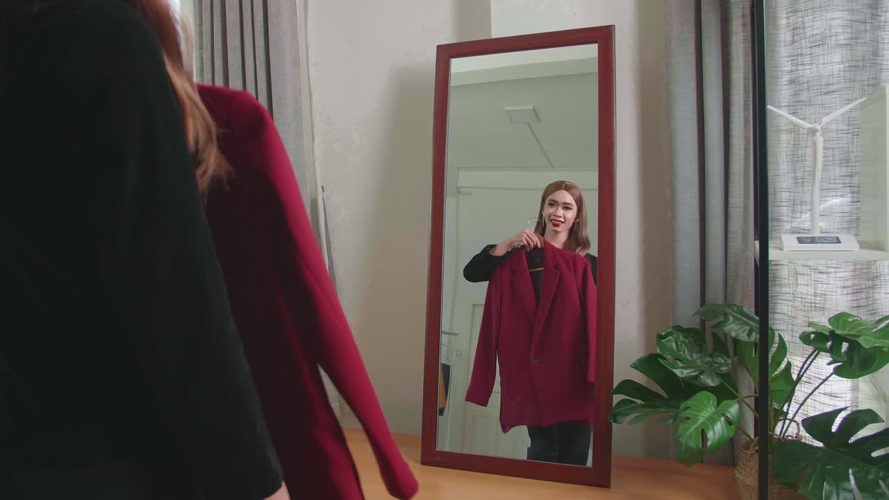 Young Transgender Woman Choosing Clothes To Wear In Front Of Mirror In Interior