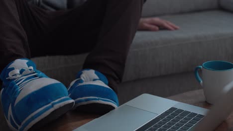 man is being lazy - sitting on couch with slippers on table next to laptop