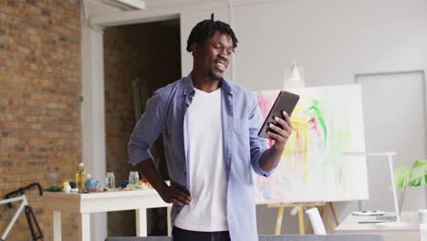Afroamerikanischer-Männlicher-Künstler-Lächelt,-Während-Er-Im-Kunststudio-Einen-Videoanruf-Auf-Einem-Digitalen-Tablet-Führt