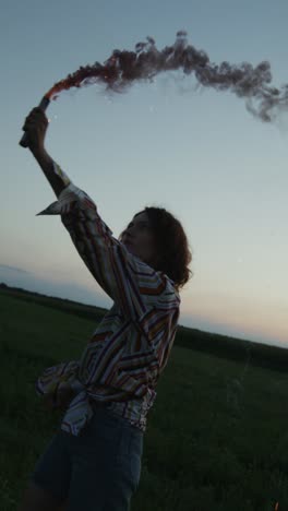 woman in field with smoke bomb at sunset