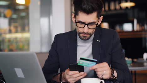 man using credit card and smartphone in a coffee shop