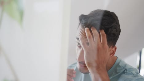 hombre biracial mirando en el espejo del baño, comprobando su cara y cabello, cámara lenta