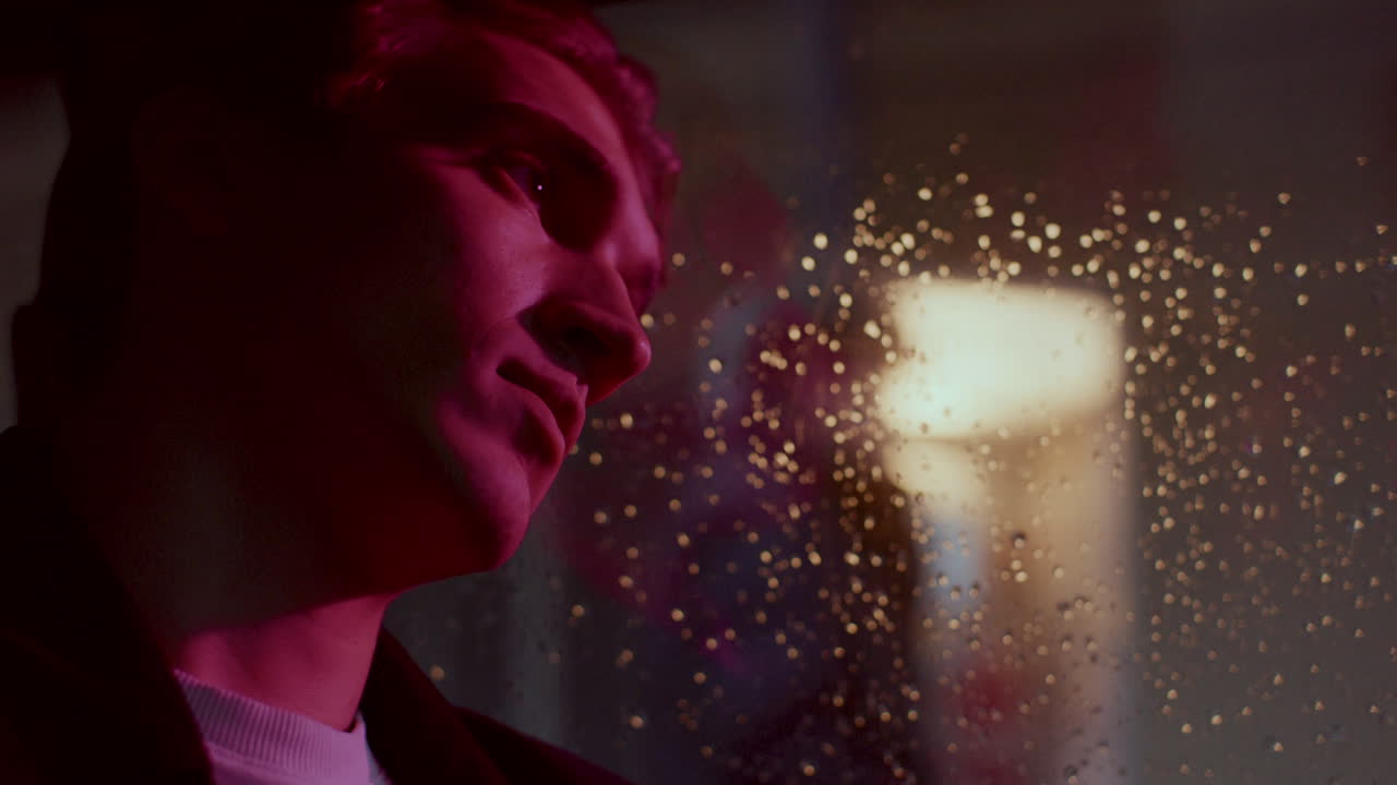 Young Contemplative Man Sitting in Car, Leaning against Window on Rainy Night