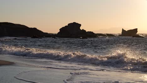 Waves-beautifully-crashing-in-slow-motion-on-wide-open-beach-with-rock-silhouettes