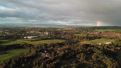 aerial video with the rainbow in a cloudy sky flying over some fields and city