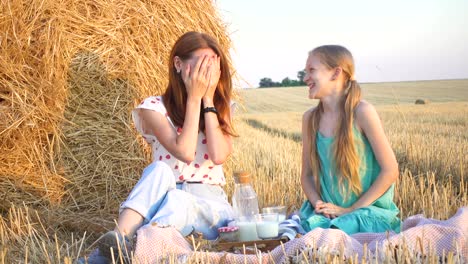 happy family in a wheat field. mother and daughter on a picnic in a wheat field near one of round bales at sunset time