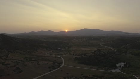 drone flying backwards with a view of a countryside rural landscape with the sun setting on top of a mountain