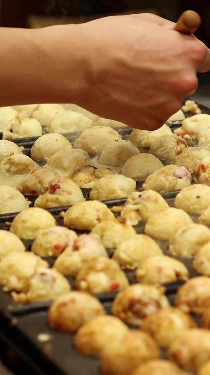 manos cocinando y girando bolas de takoyaki en una parrilla