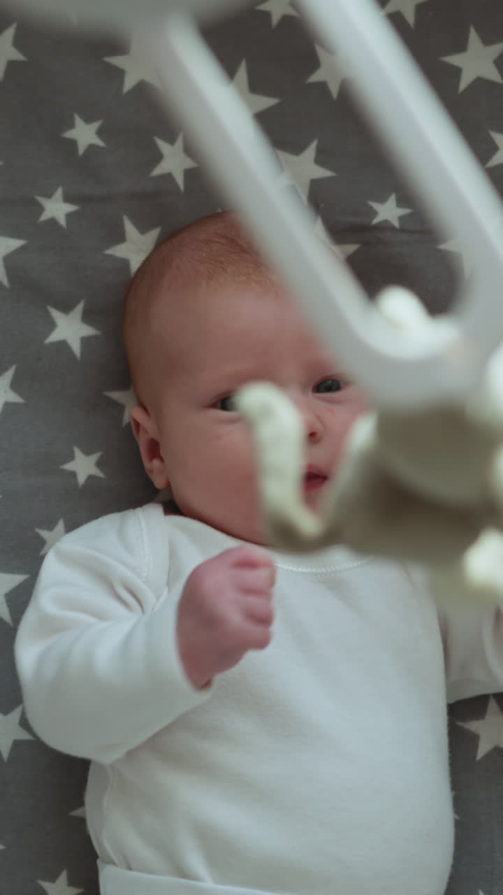 Primo piano di un neonato innocente con gli occhi azzurri che indossa una tutina bianca, sdraiato su una coperta con motivo a stelle.
