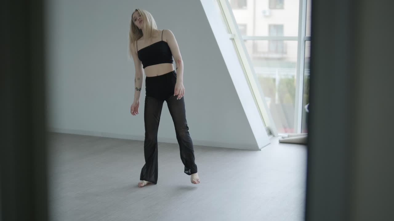 Ballerina in abiti neri che esegue danza contemporanea. Movimenti fluidi e aggraziati in una stanza bianca. Coreografia di balletto moderno.