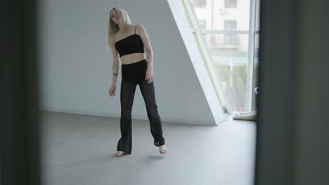 fit girl in black clothes performing contemporary. female dancer shows flowing motions, body and hands waves at white room. modern ballet dance choreography. young woman is moving smoothly