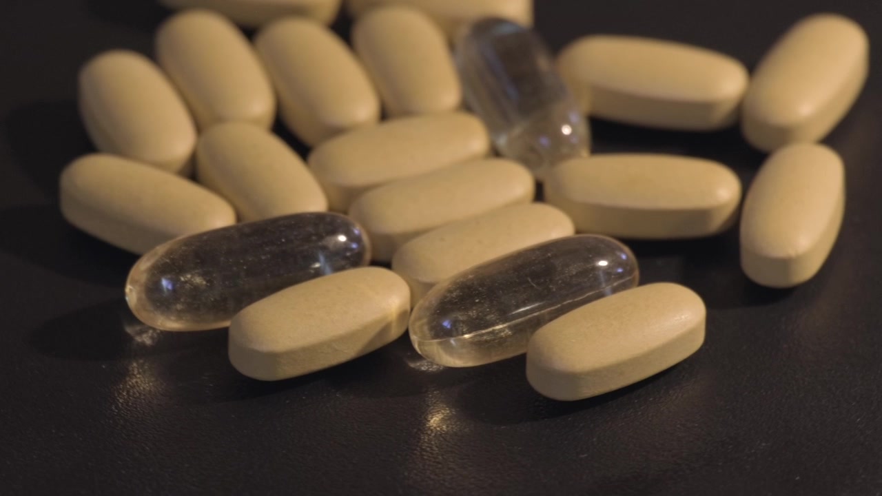 Primo piano di pillole beige mescolate con softgel trasparenti su una superficie scura