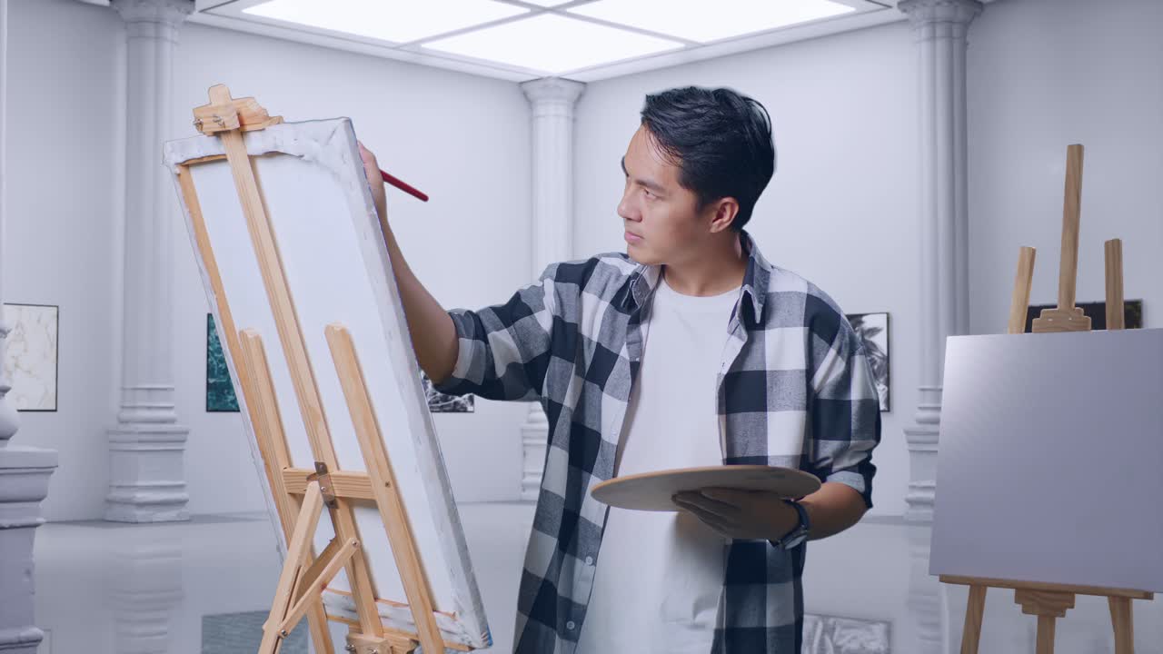 아시아 남성 예술가는 갤러리에서 오일 페인트와 으로 캔버스에 그림을 그리는 데 집중하고 있습니다.