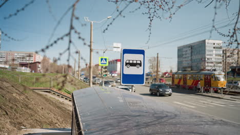 city view featuring a bus stop sign, traffic, and a tram on a sunny day , with cars passing, with clear blue skies and a lively atmosphere