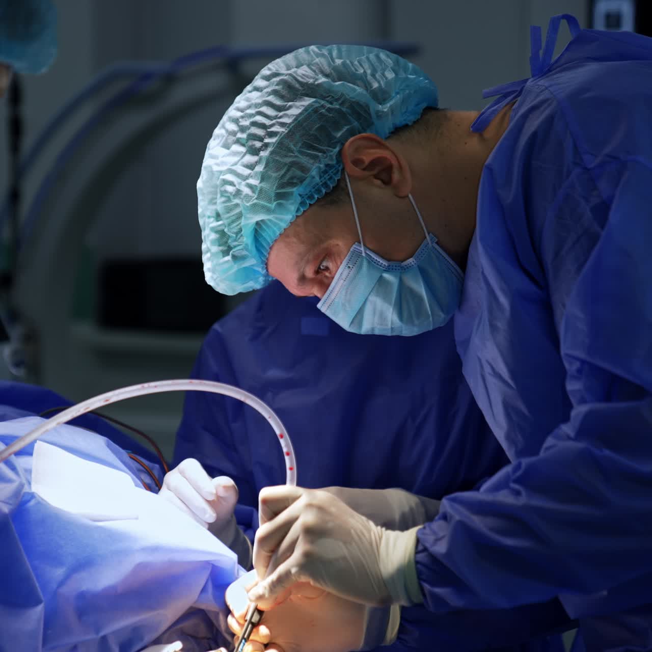 Attentive male neurosurgeon bent over the patient using metal and electric tools and devices. Assisting medics stand on both sides of a surgeon