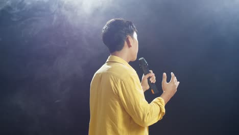 back view of a young boy holding a microphone and singing on the white smoke black background