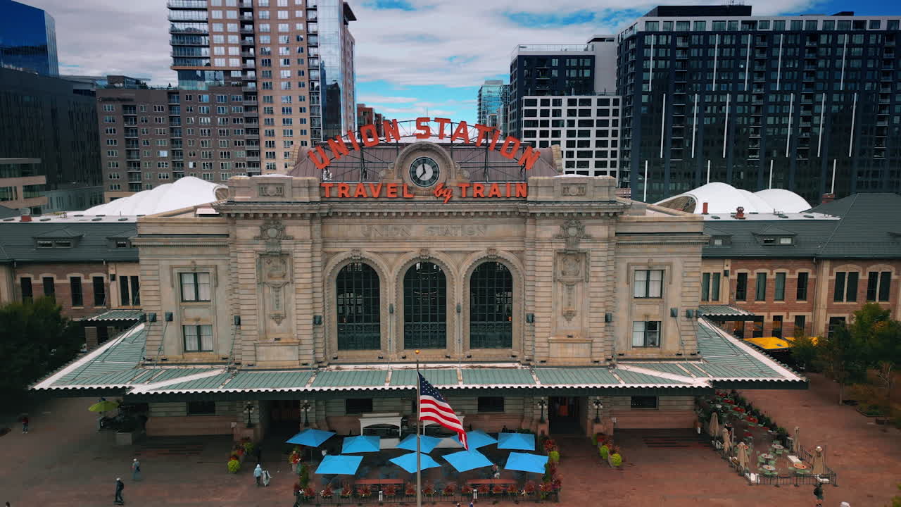 Denver, USA, 28 July 2025: Beautiful building of the railway Union Station in Denver, Colorado, USA. People walk into and out of the buildings. Drone footage rising over the square in front of the station