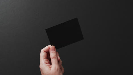 Hand-of-caucasian-woman-holding-black-business-card-on-black-background,-copy-space,-slow-motion