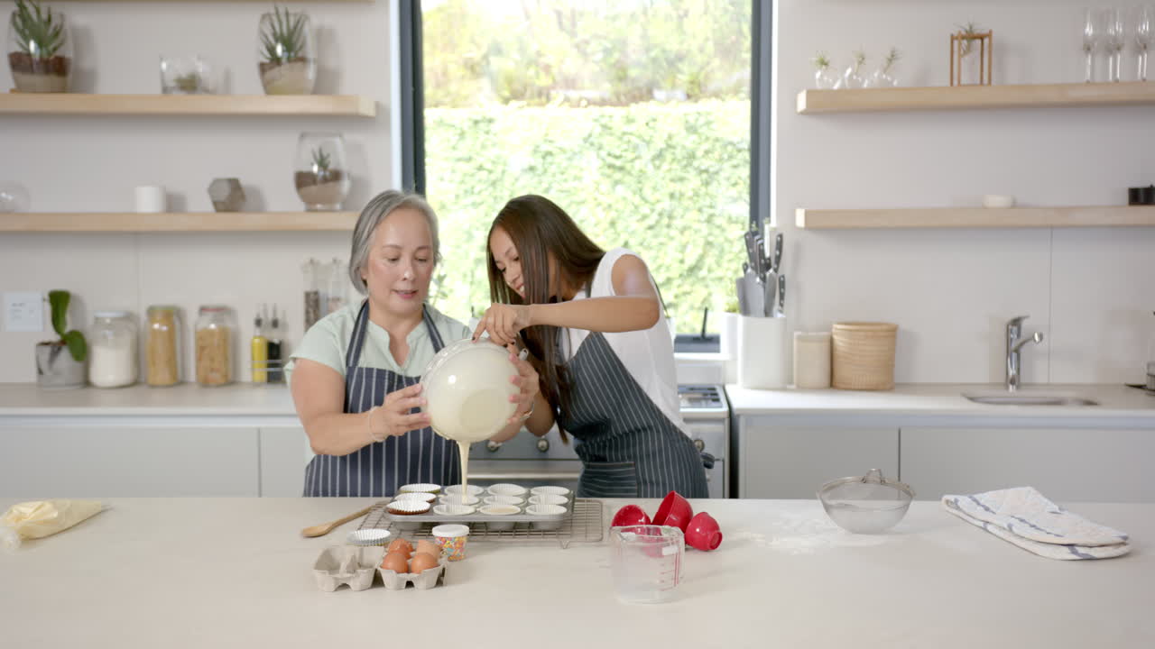 Baking cupcakes, asian grandmother and granddaughter pouring batter into tray in kitchen
