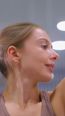 primer plano de una mujer joven haciendo ejercicio, realizando ejercicios de estiramiento profundo con luces de techo bokeh suaves, sonríe cálidamente, centrado en la flexibilidad y el movimiento en un brillante