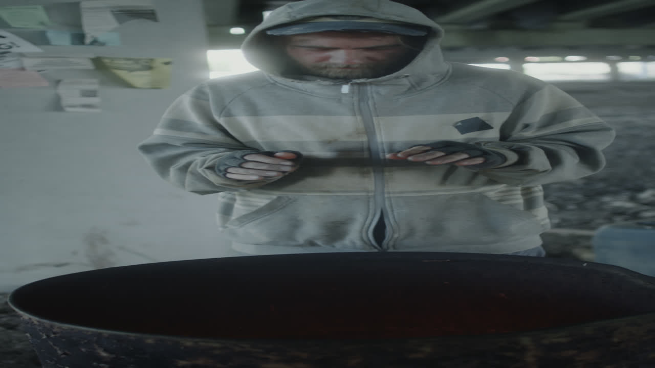 Man warming hands by a barrel fire