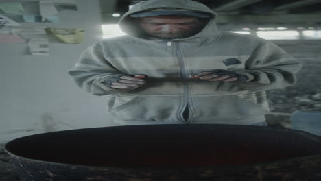 man warming hands by a barrel fire