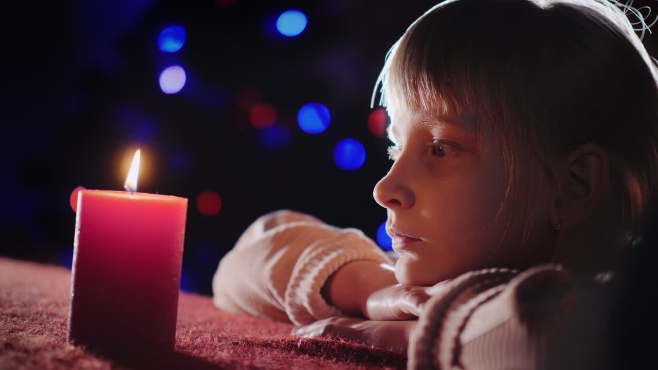 retrato de perfil de una niña mira una vela encendida y la lanza en la víspera de navidad