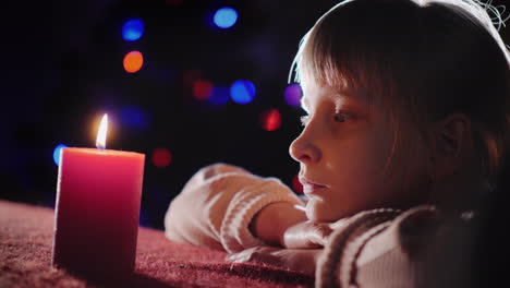 retrato de perfil de una niña mira una vela encendida y la lanza en la víspera de navidad