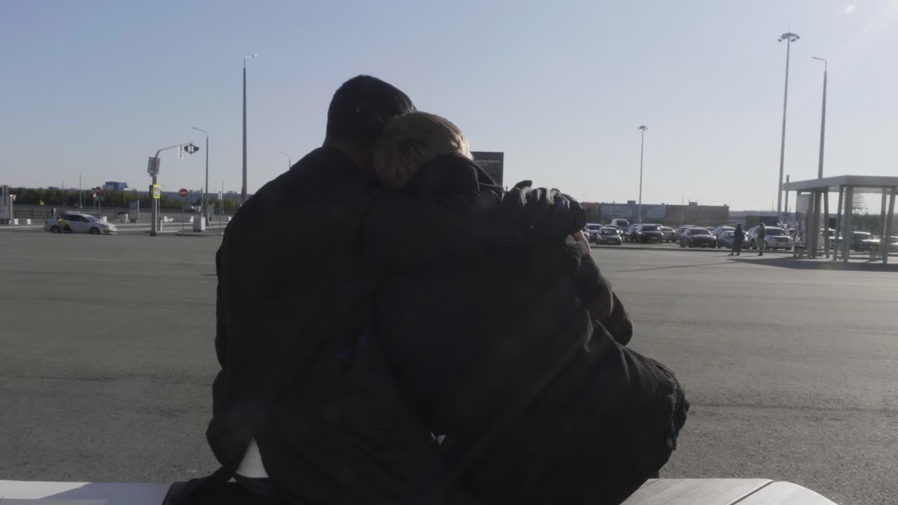 una pareja abrazándose en el estacionamiento del aeropuerto.