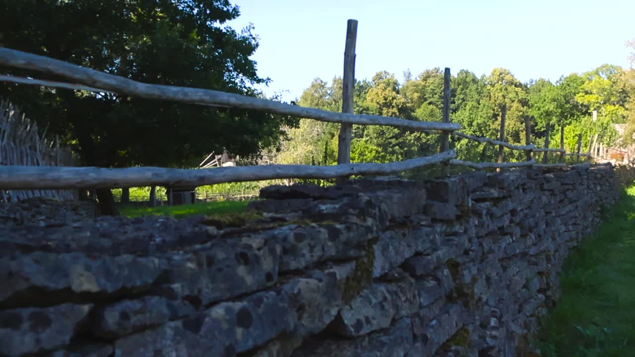 Gorgeous old and traditional limestone mossy dry stone wall in a sunny summer garden with some wooden poles and sticks on it to make it higher. Green forest and trees in the background