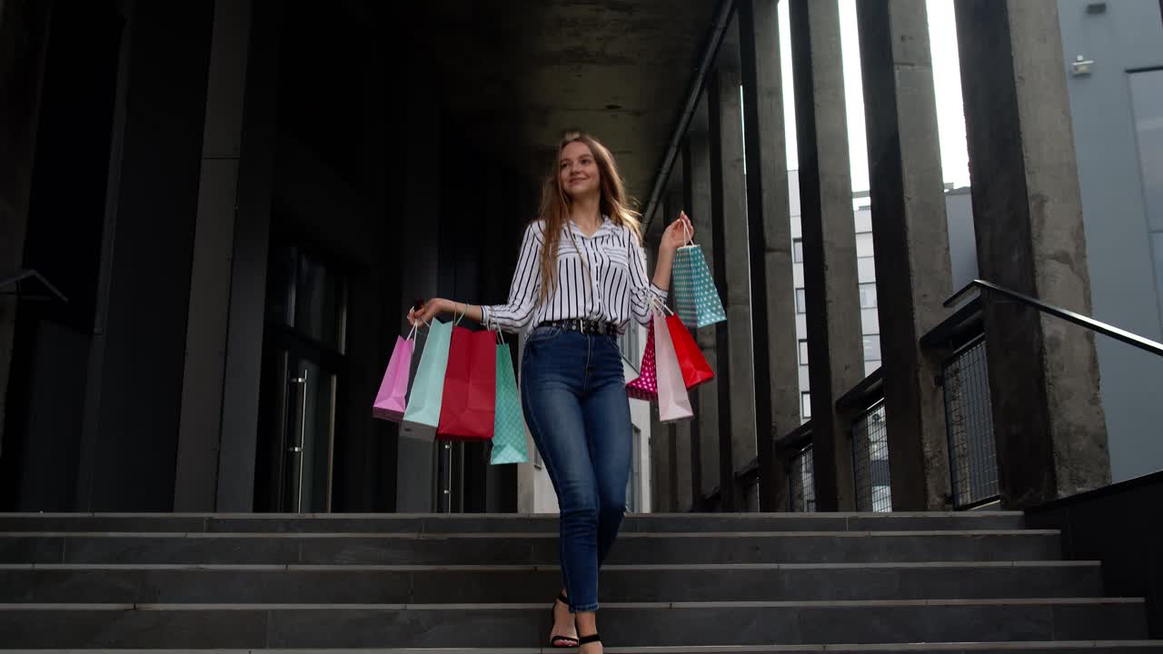 chica sonriente caminando desde el centro comercial con bolsas de compras, feliz con los precios bajos en el viernes negro