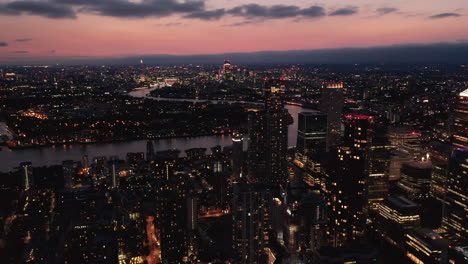 Forwards-fly-above-night-town.-Illuminated-streets-and-buildings.-Cityscape-against-colourful-sky-after-sunset.-London,-UK