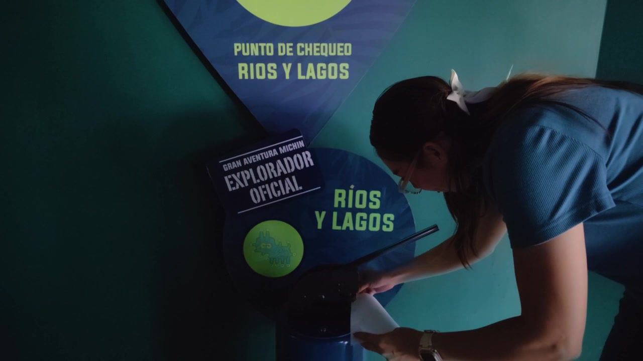 Uma jovem mulher latina é vista carimbando uma folha de papel branca no posto de controle "Rios y Lagos" dentro do Acuario Michin na Cidade do México. Ela está completando uma atividade no aquário