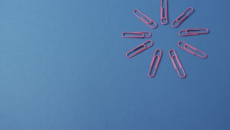 Close-up-of-pink-paper-clips-in-circle-and-copy-space-on-blue-background