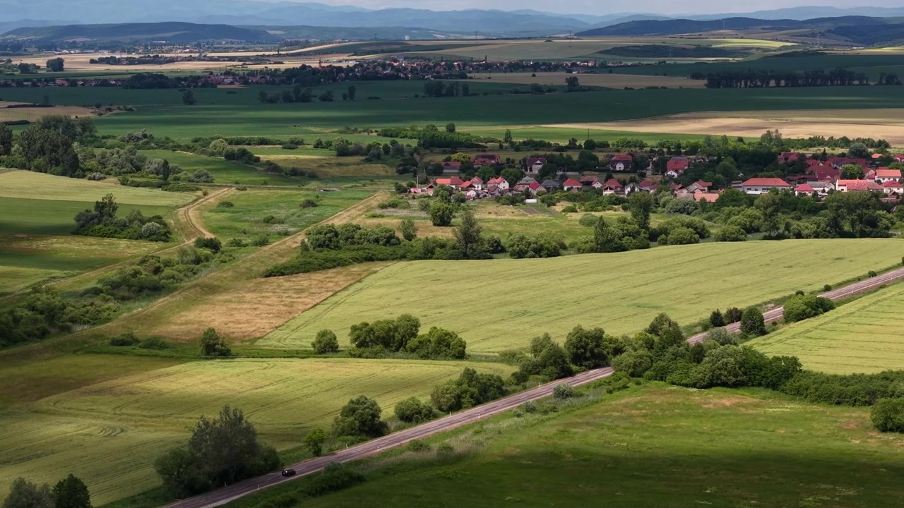 En forhøyet utsikt fanger det vakre ungarske landskapet, med store grønne jorder, en fredelig landsby og majestetiske fjell i det fjerne.