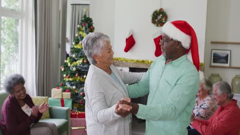 Glückliches,-Vielfältiges-älteres-Paar,-Das-Zur-Weihnachtszeit-Zusammen-Mit-Freunden-Im-Hintergrund-Tanzt