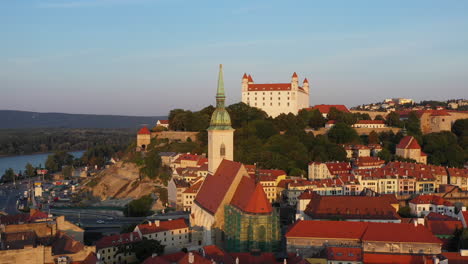 Amplia-Rotación-De-Drones-Con-La-Catedral-De-San-Martín-En-Primer-Plano-Y-El-Castillo-De-Bratislava-En-El-Fondo-En-Bratislava-Eslovaquia-Durante-La-Puesta-De-Sol