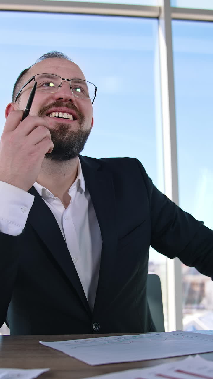 Smiling entrepreneur in office. Portrait of a businessman in glasses sitting at the table with a laptop. Office worker indoors. Vertical video